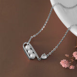 Silver necklace with three pearls and a heart pendant on a brown surface.