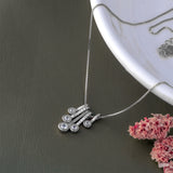 Silver necklace with a unique pendant on a dark surface with pink flowers.