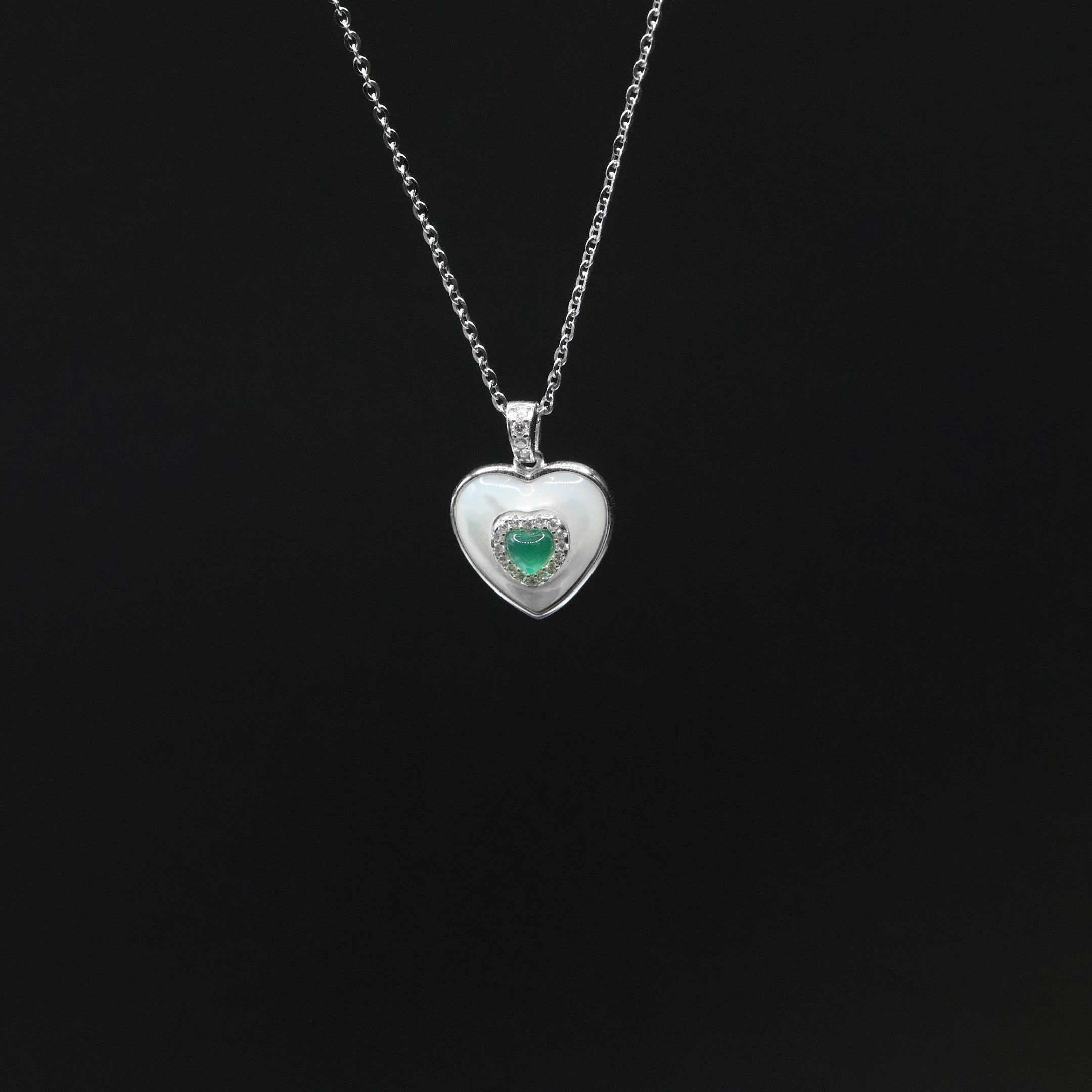 Heart-shaped silver pendant with a green gemstone on a black background