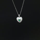 Heart-shaped silver pendant with a green gemstone on a black background