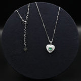 Two silver necklaces with heart-shaped pendants on a black circular stand.