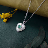 Silver heart-shaped necklace with a green gemstone on a textured surface with yellow flowers.