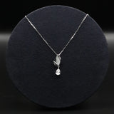 Silver necklace with a leaf and teardrop pendant on a black background
