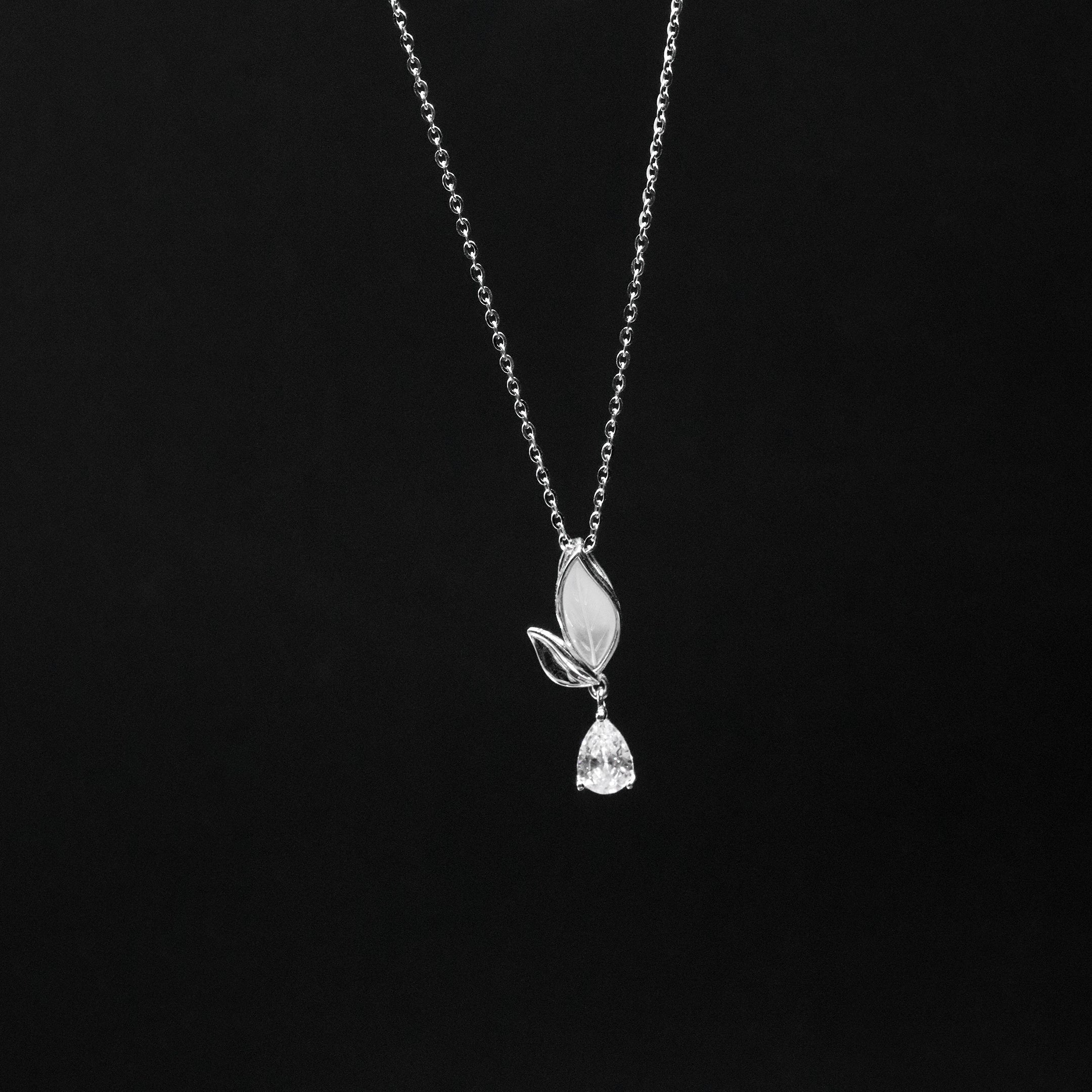 Silver necklace with a leaf and teardrop pendant on a black background