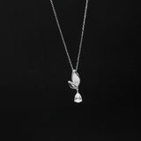 Silver necklace with a leaf and teardrop pendant on a black background