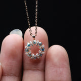 Small circular pendant with gemstones held between fingers against a black background