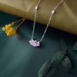 Necklace with a pink pendant on a textured surface with yellow flowers and green leaves.