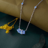 Silver necklace with a blue pendant on a textured surface with yellow flowers.