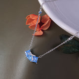 Necklace with a blue pendant on a dark surface with flowers in the background