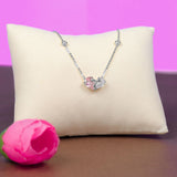Necklace with a heart-shaped pink and clear pendant on a beige pillow against a purple background