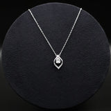 Silver necklace with a teardrop-shaped pendant on a black textured surface