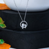 Silver necklace with a circular pendant featuring two birds on a black stand.