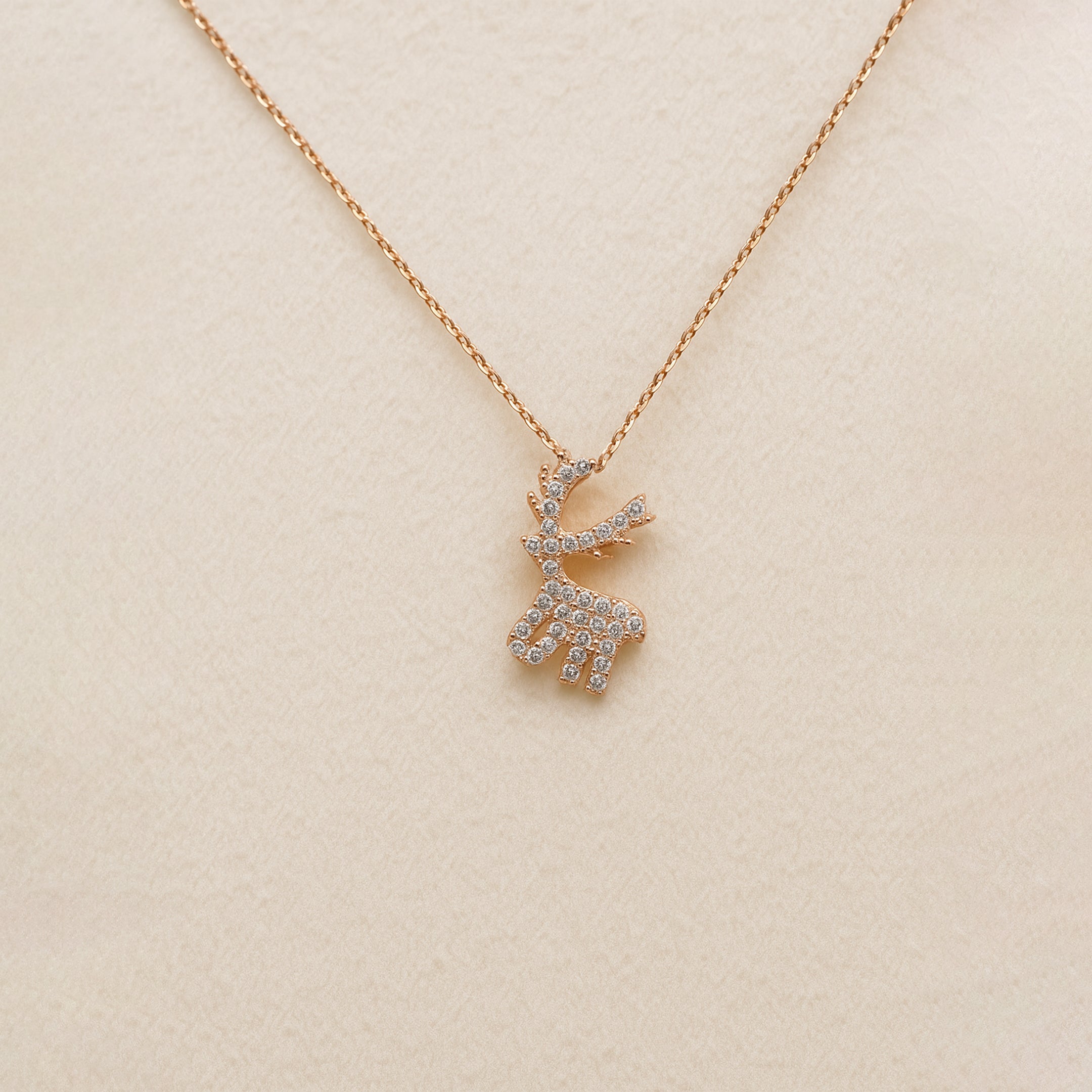 Rose gold deer-shaped necklace with diamonds on a beige background
