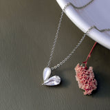 Silver necklace with a heart-shaped pendant next to a pink flower on a gray surface.