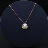 Gold necklace with a round pendant featuring a pearl on a dark blue cushion