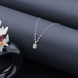 Silver necklace with a diamond pendant on a dark surface with flowers.