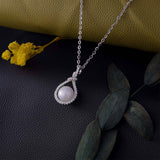 Pearl necklace with silver chain on a dark surface with yellow flowers and green leaves.