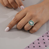 Hand wearing a ring with a green gemstone on a light background
