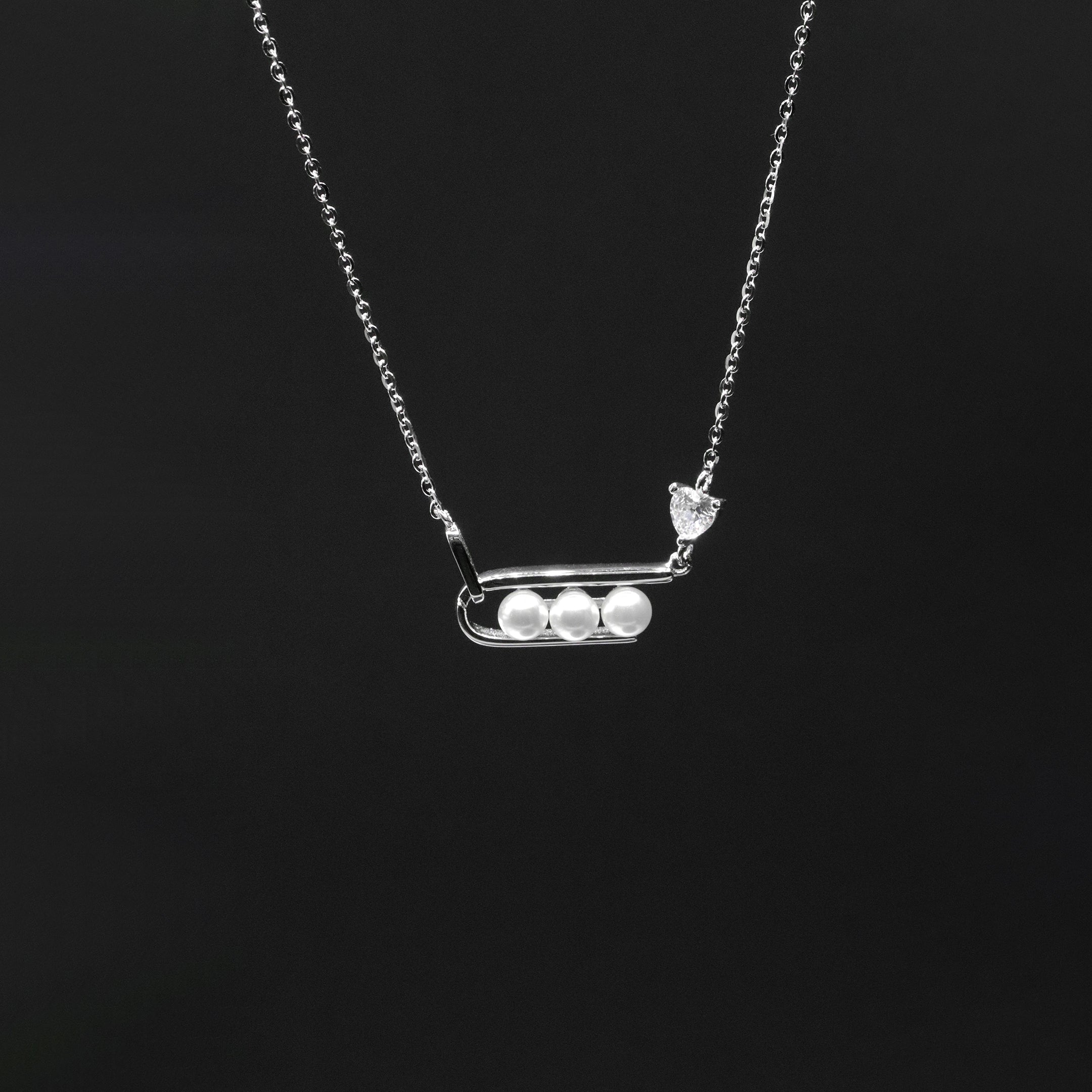 Silver necklace with a heart and three pearls on a black background