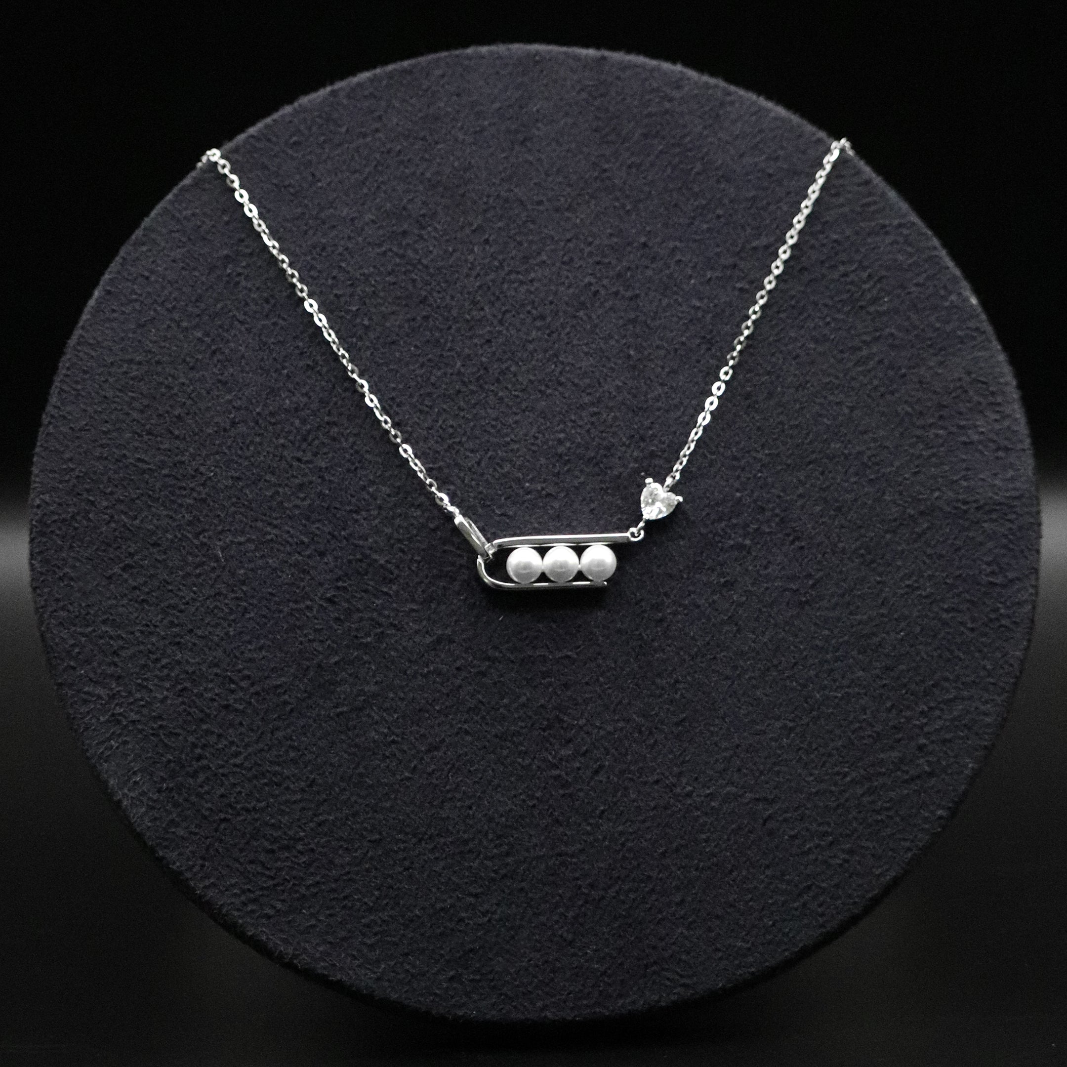Silver necklace with three pearls on a black circular stand