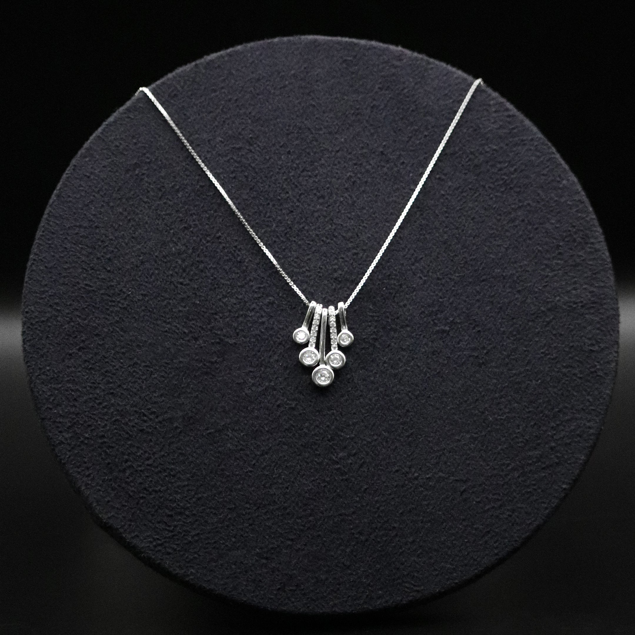 Silver necklace with a pendant on a black circular stand