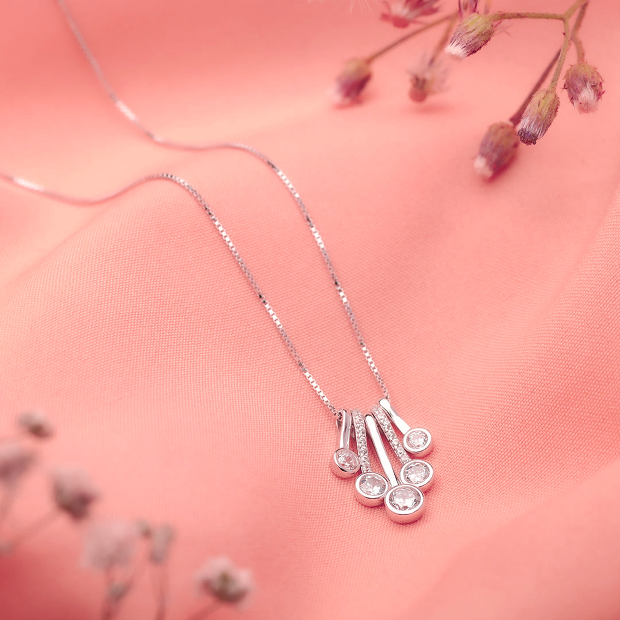 Silver necklace with a decorative pendant on a pink background