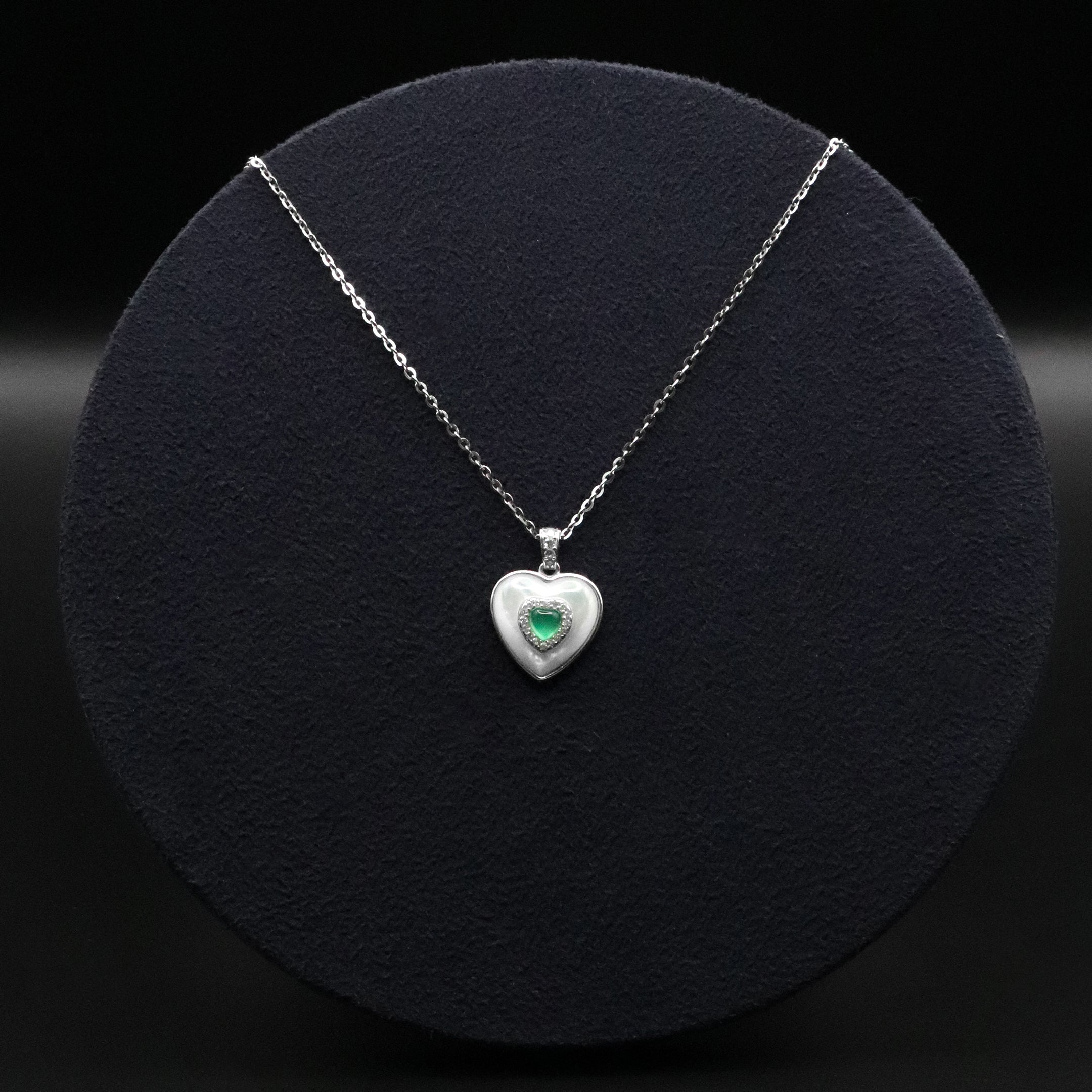 Heart-shaped silver pendant with a green gemstone on a black background