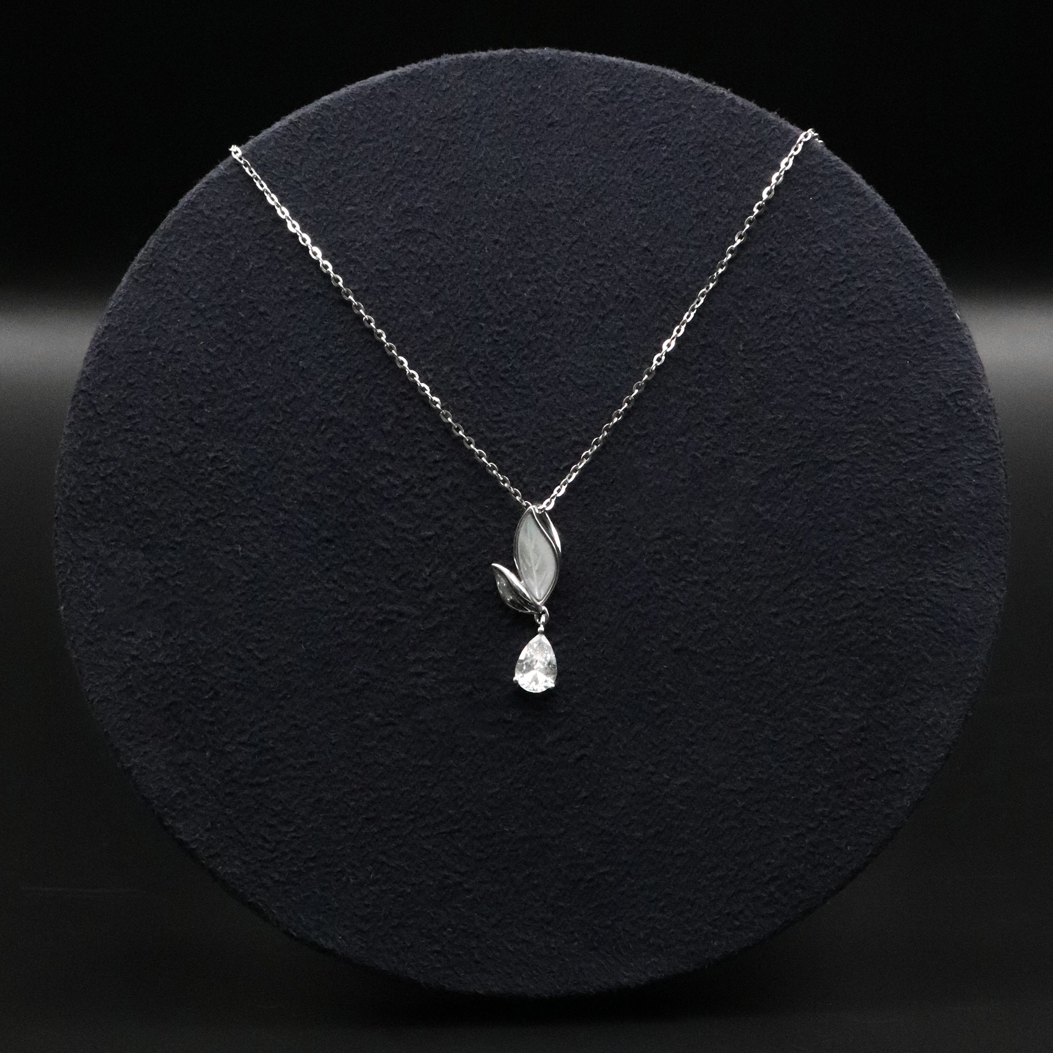 Silver necklace with a leaf and teardrop pendant on a black background