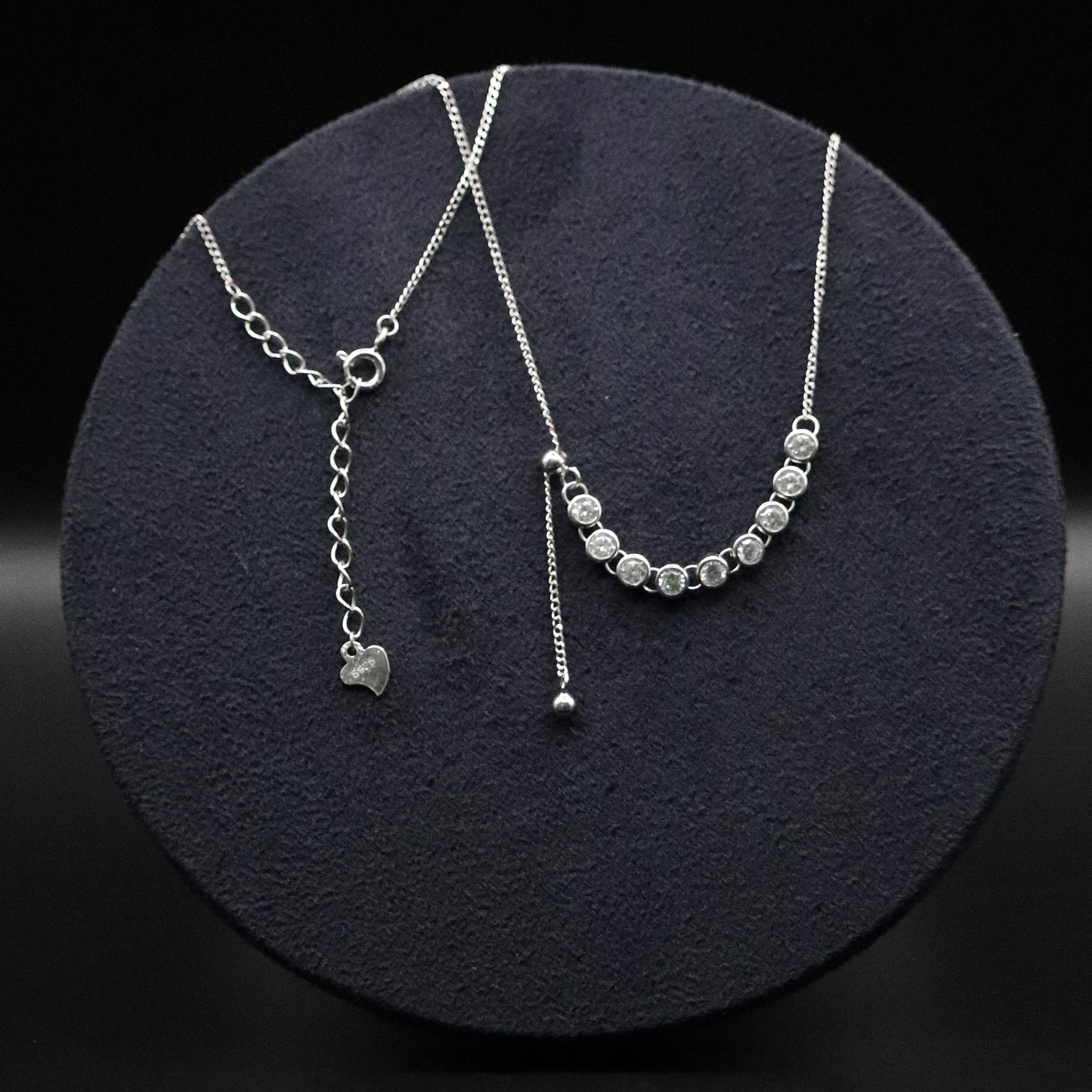 Silver necklace with heart charm and beaded extension on a dark round surface