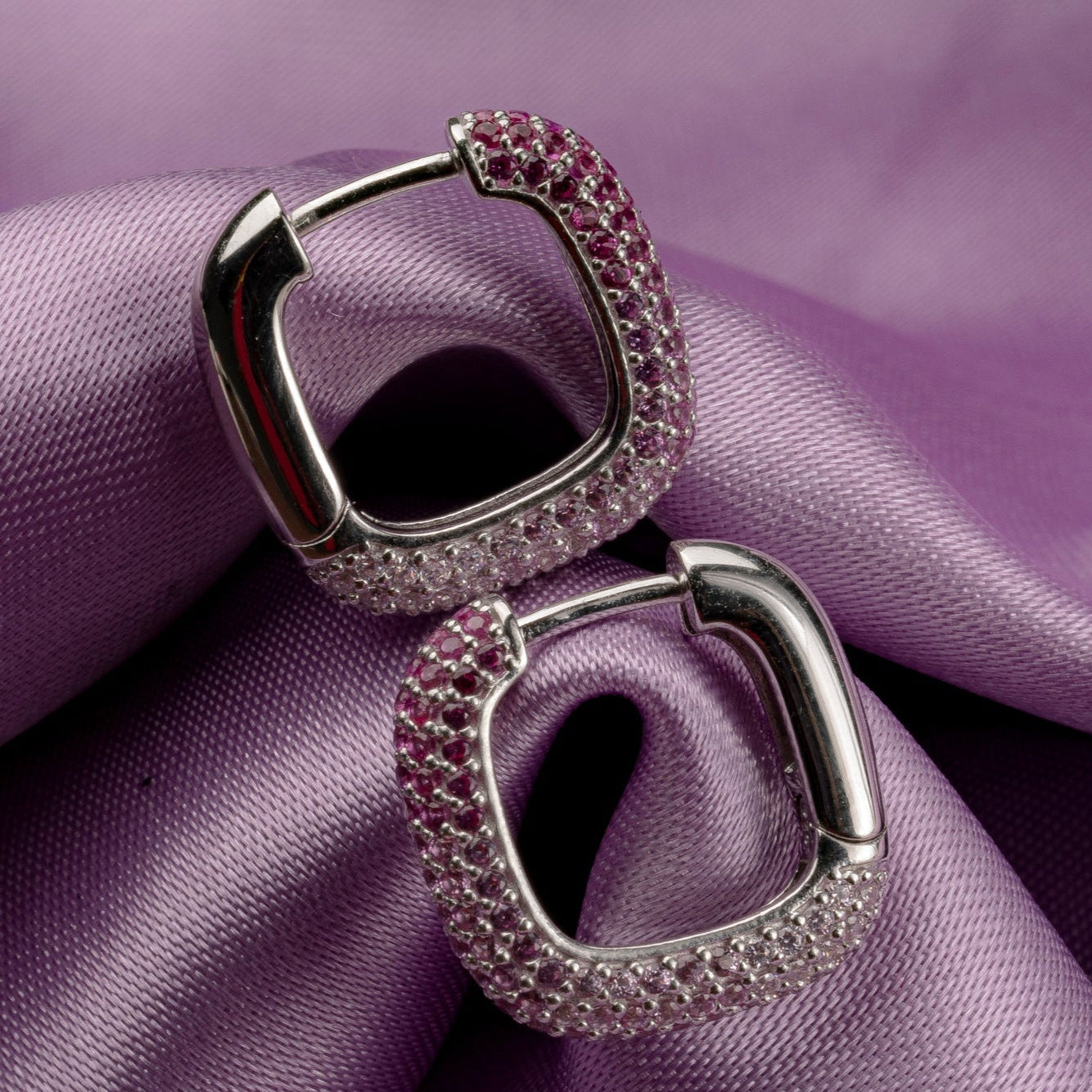 Pair of silver earrings with pink gemstones on a purple fabric background
