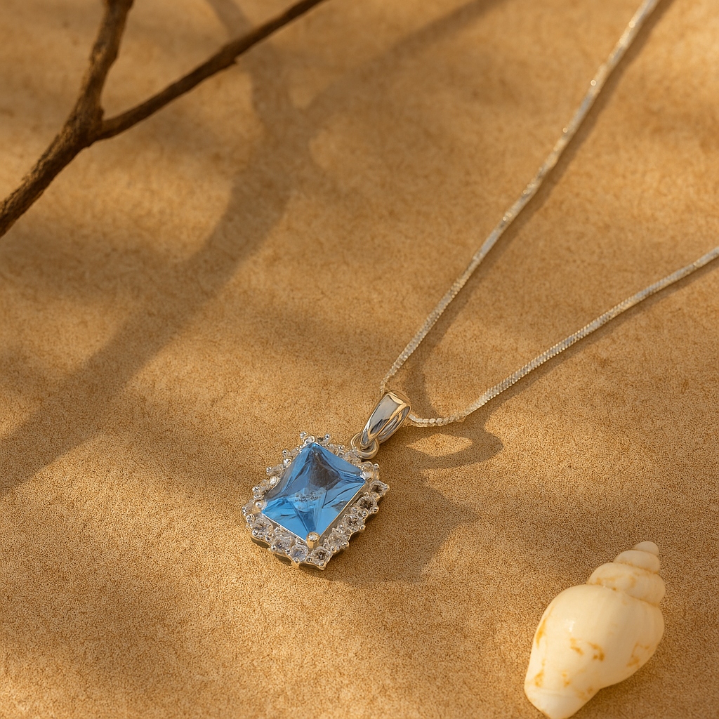Silver necklace with a blue pendant on a sandy surface with a shell.