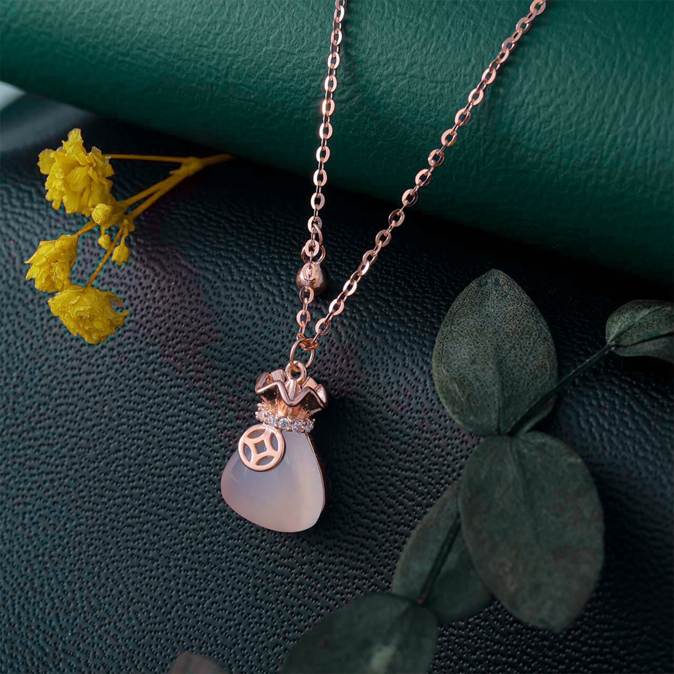 Necklace with a pendant on a textured surface with yellow flowers and green leaves.