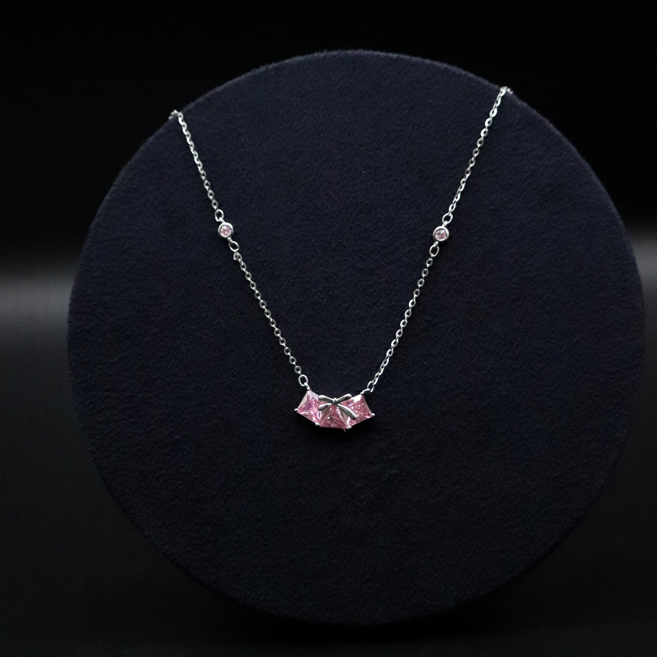 Silver necklace with a pink pendant on a black background