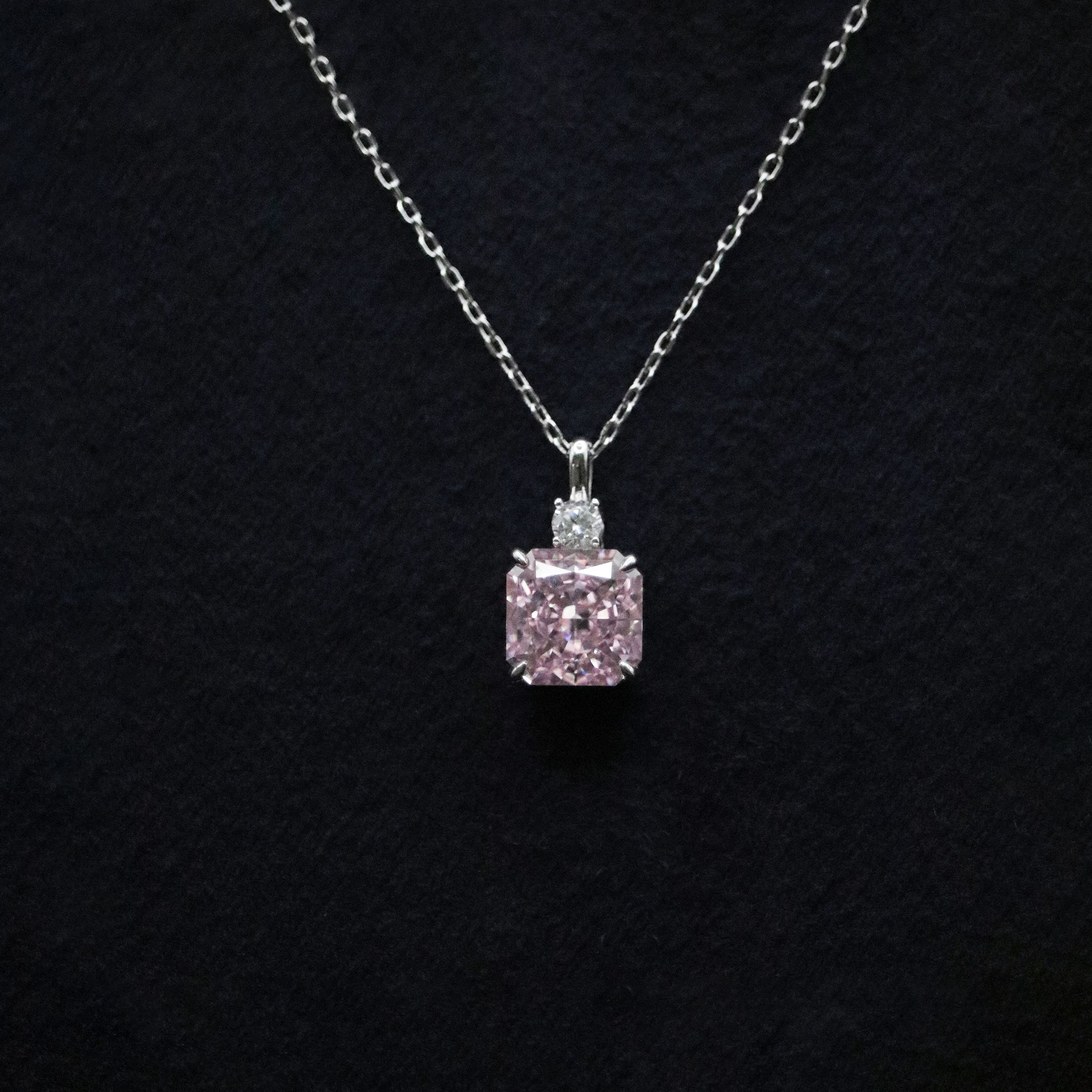 Pink diamond pendant on a chain against a black background