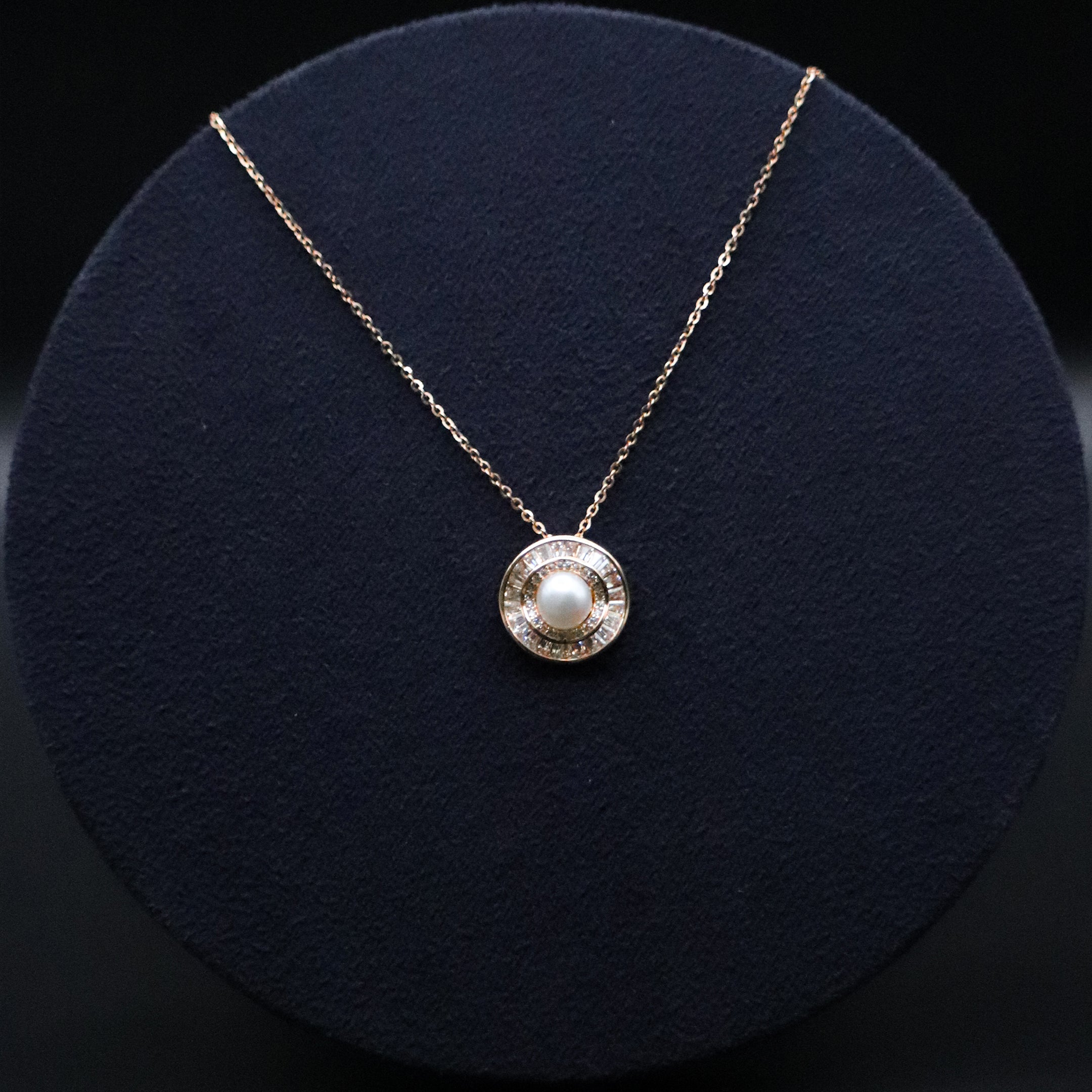 Gold necklace with a round pendant featuring a pearl on a dark blue cushion