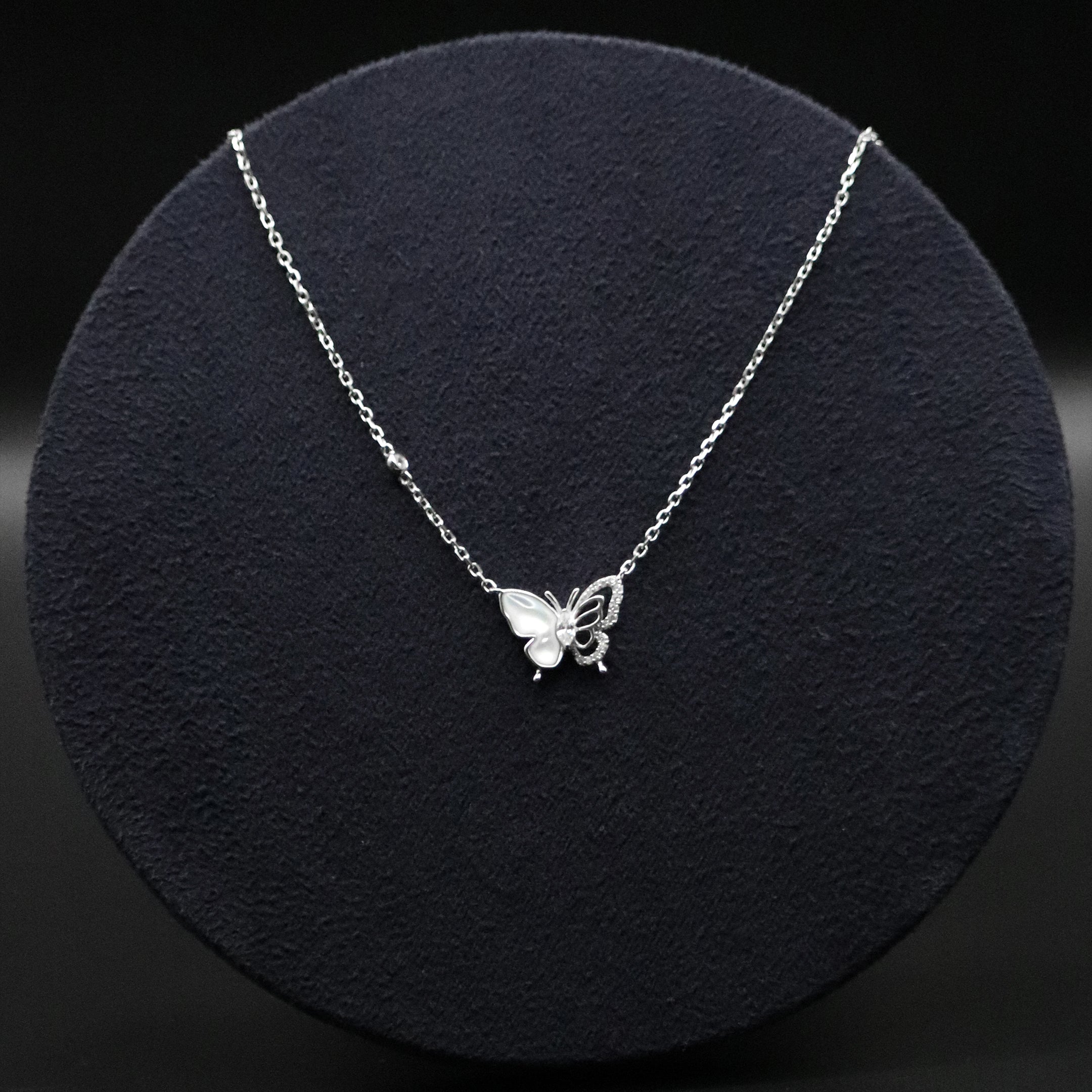 Silver butterfly necklace on a black textured stand