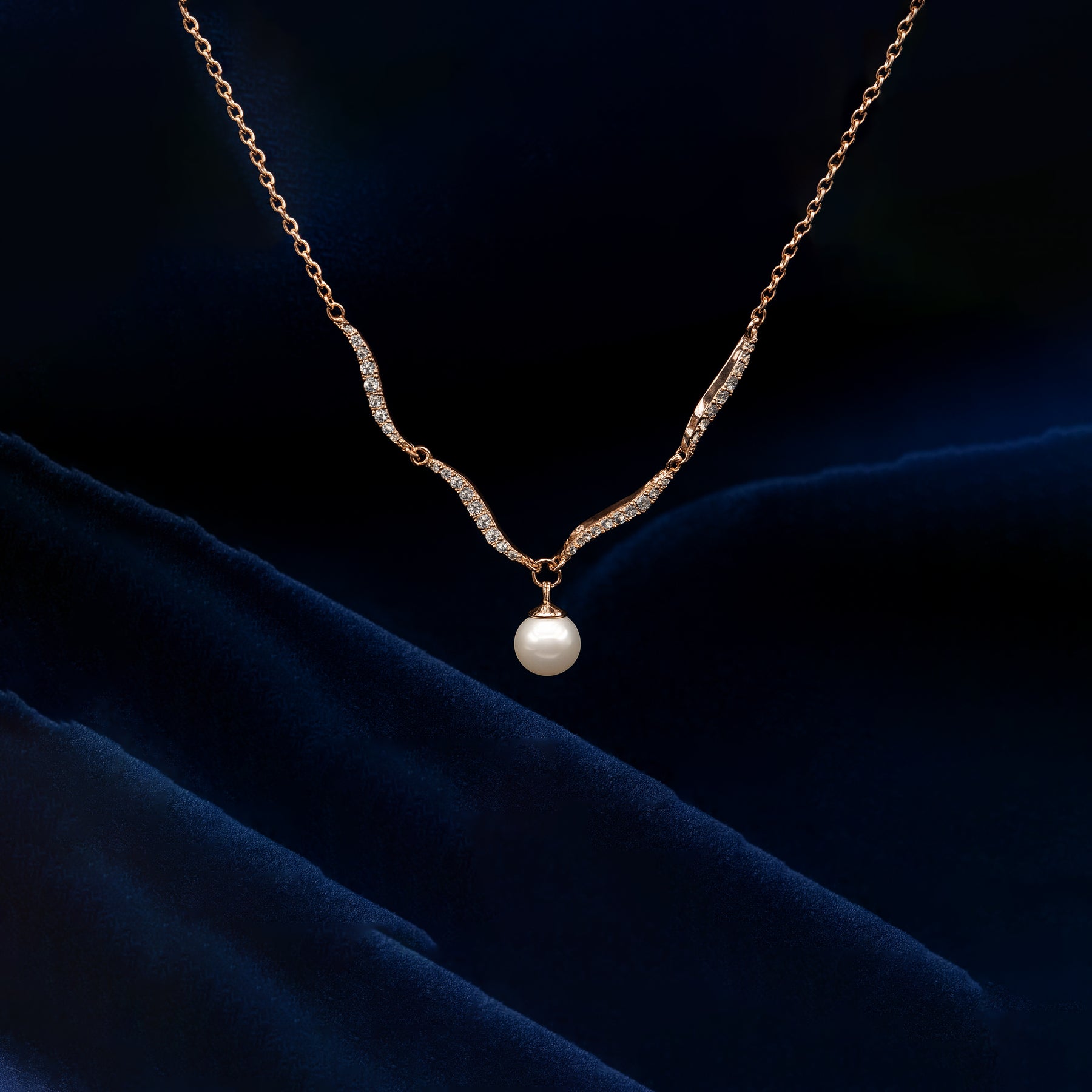 Gold necklace with a pearl pendant on a dark blue fabric background