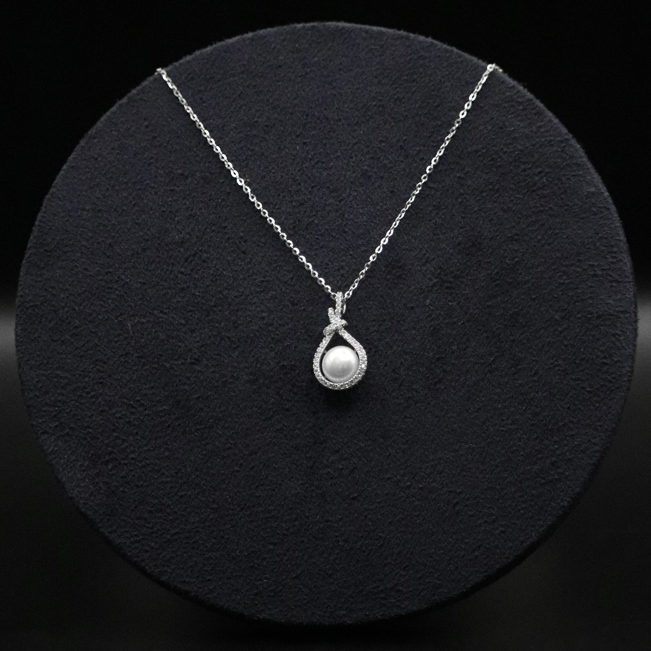 Silver necklace with a pearl pendant on a black textured surface