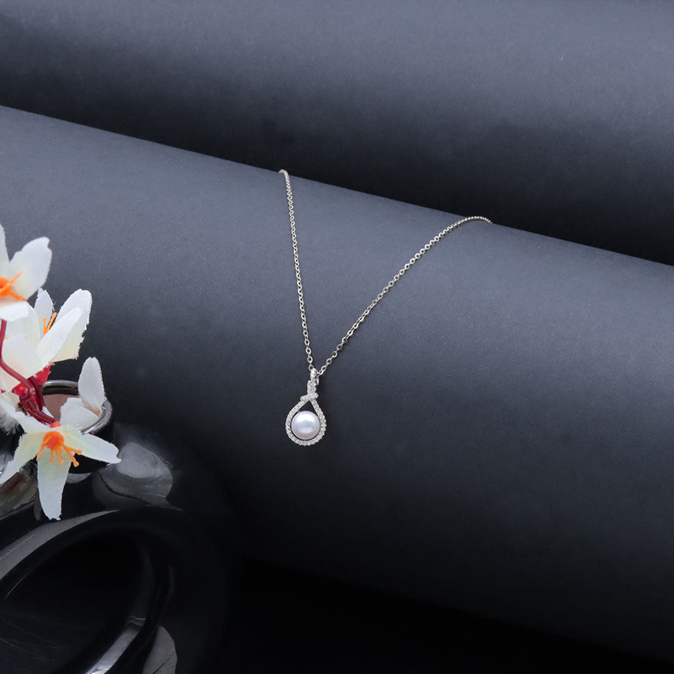 Pearl necklace on a dark surface with flowers in the background