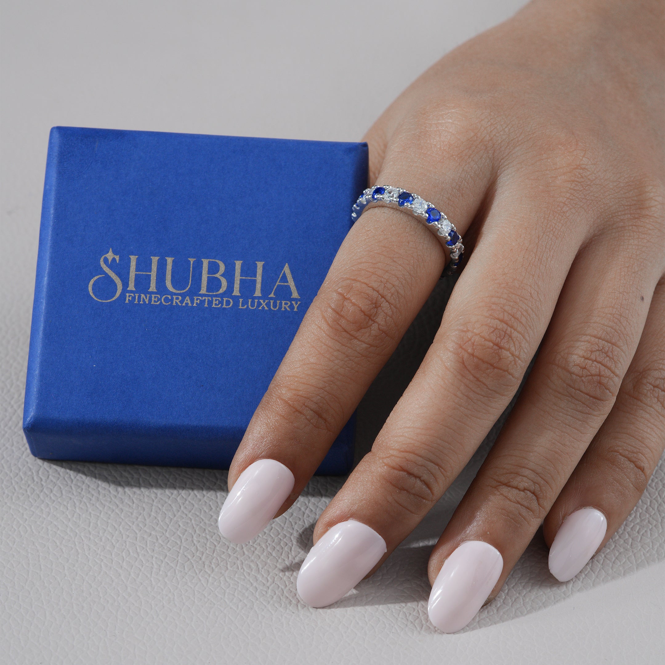 Hand wearing a ring with a blue gemstone next to a Shubha jewelry box