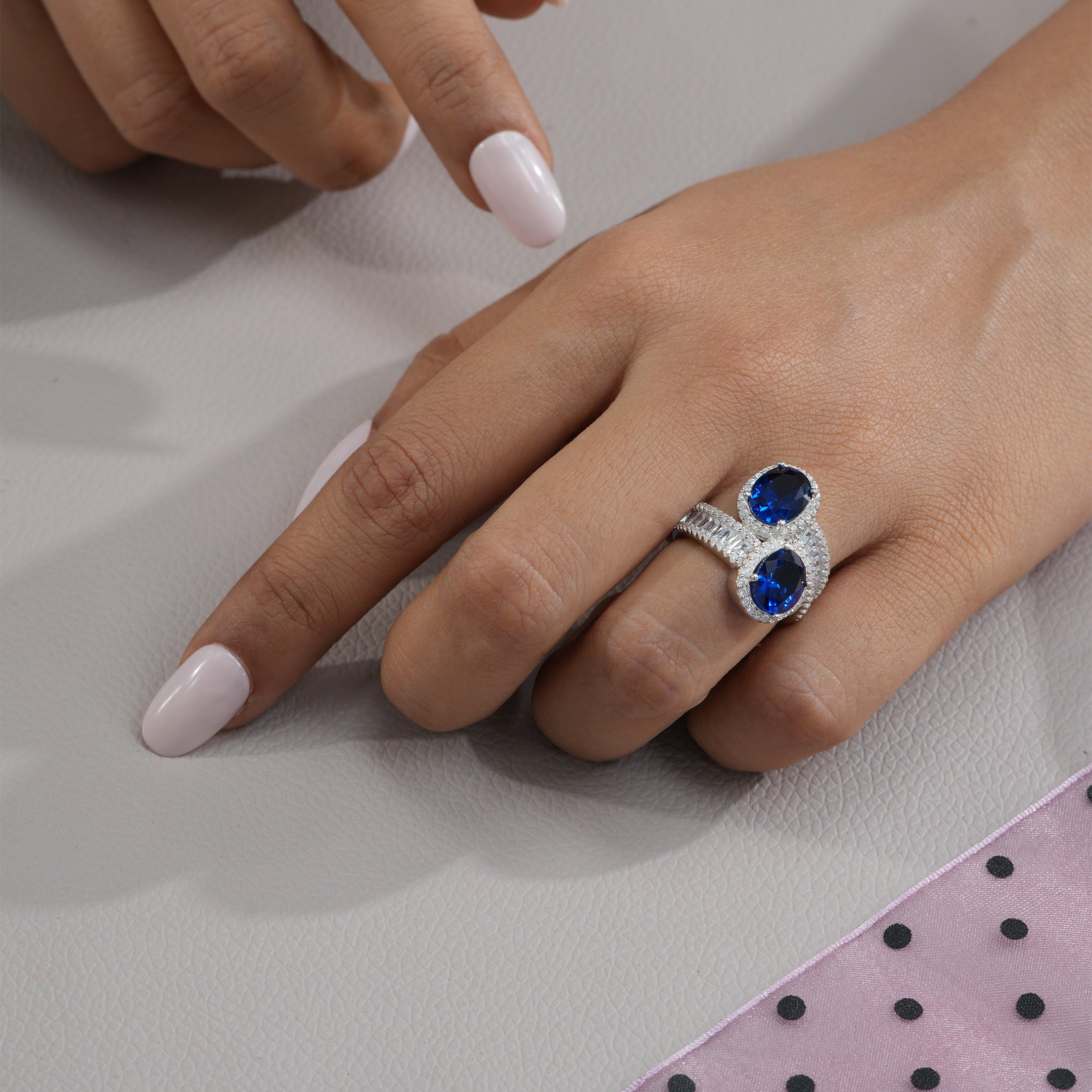 Hand wearing a silver ring with blue gemstones on a light background