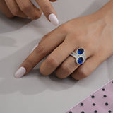 Hand wearing a silver ring with blue gemstones on a light background