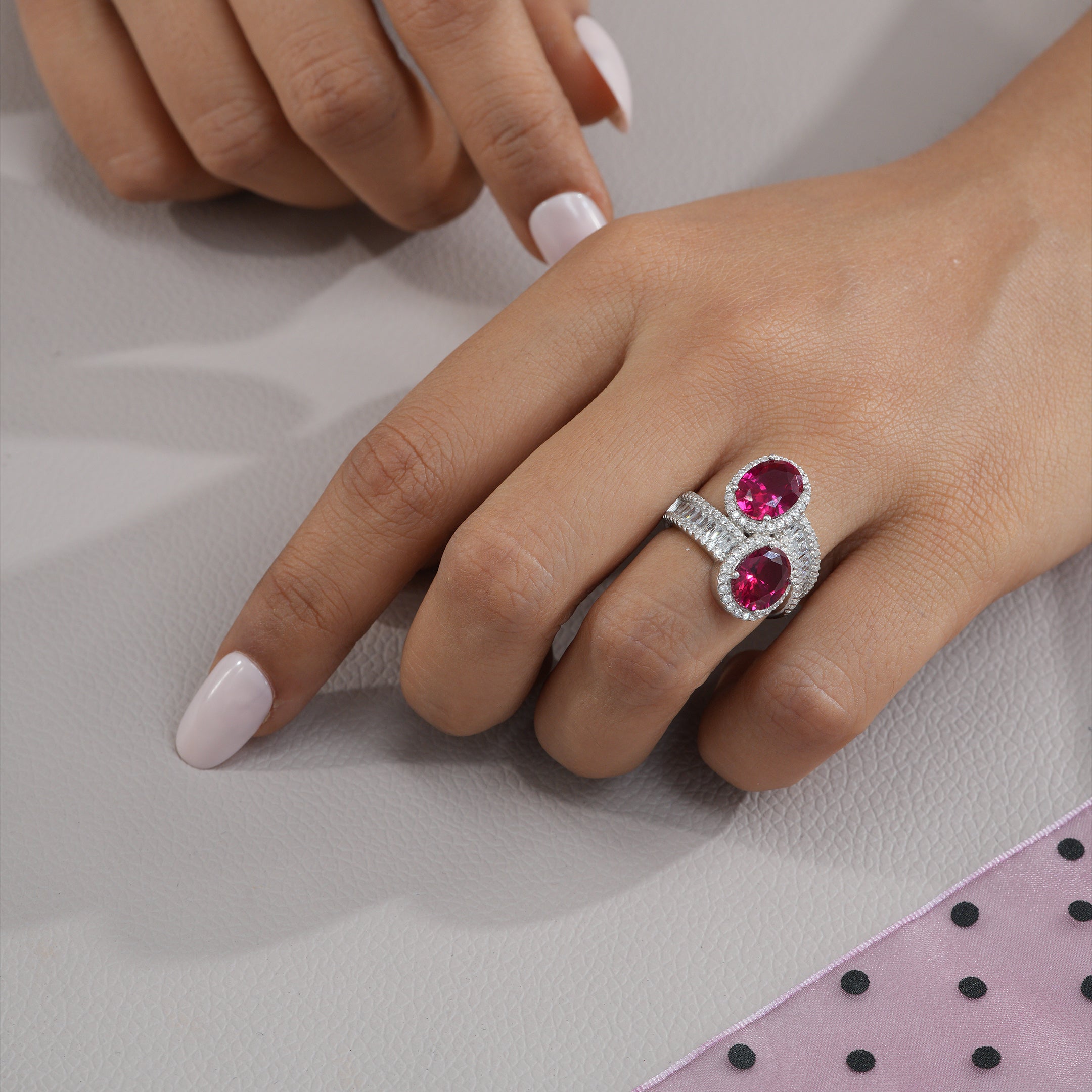 Close-up of a hand wearing a ring with pink gemstones on a light background