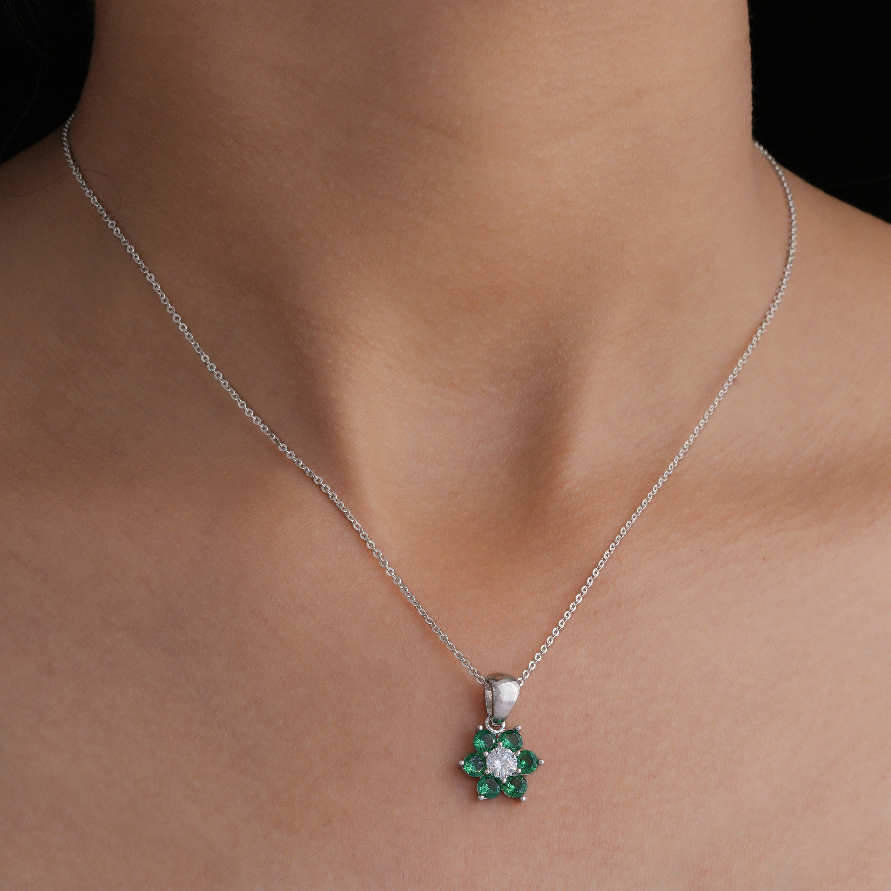 Silver necklace with a green gemstone pendant on a person's neck against a black background