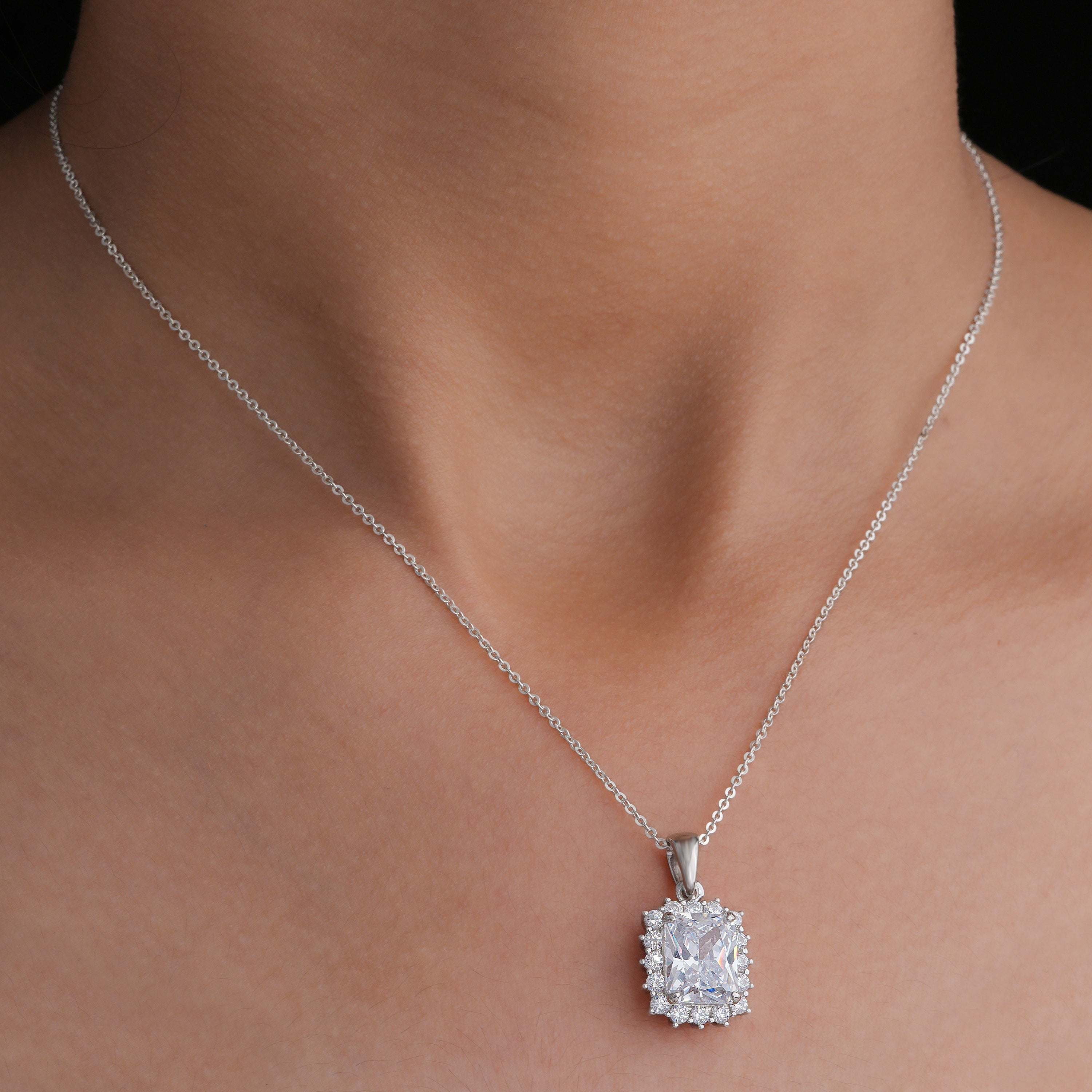 Silver necklace with a diamond pendant on a person's neck against a neutral background