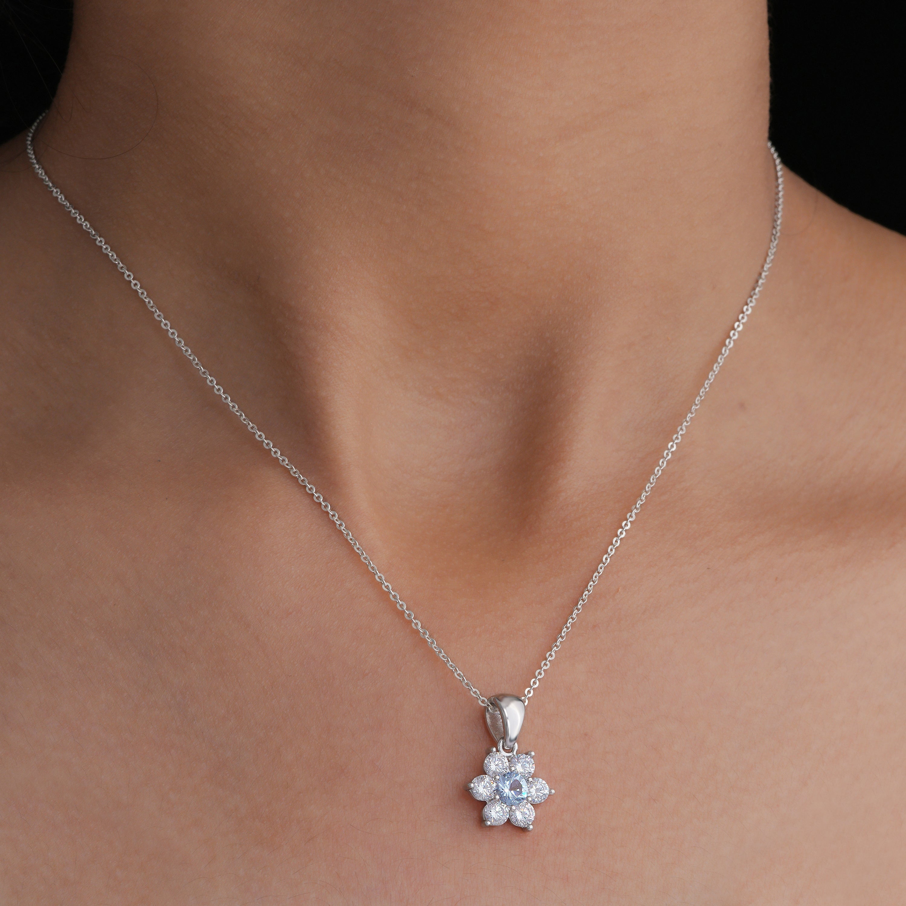 Silver necklace with a floral pendant on a person's neck against a neutral background