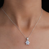 Silver necklace with a floral pendant on a person's neck against a neutral background